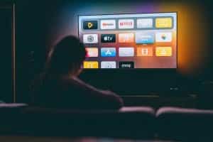 Person seated on a couch watching tv, movies, and YouTube. Watching tv to learn spanish and other languages is one language learning method.